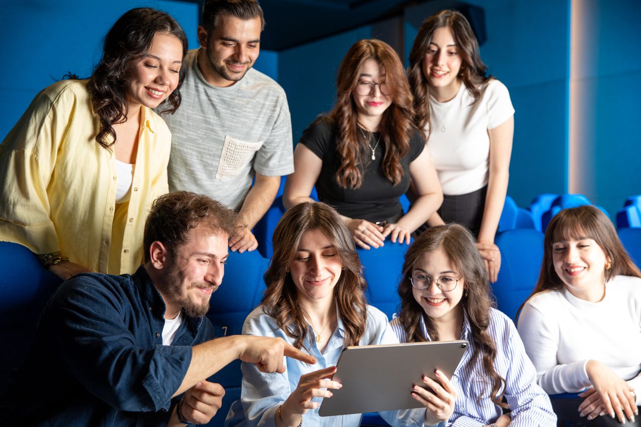 Mastering the First Impression: Your intriguing post title goes here Group of young adults enthusiastically interacting with a tablet in an indoor setting.