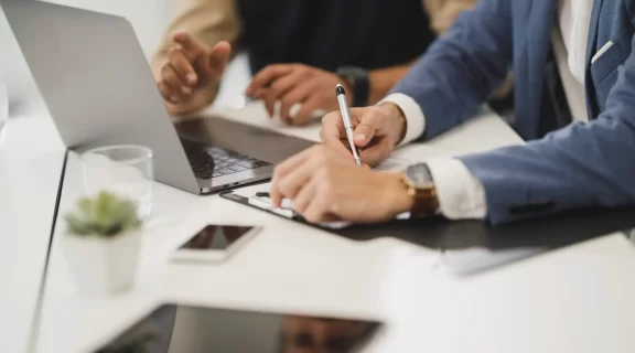 Free close up of two people hands, signing documents with laptop on table in office image, public domain CC0 photo.
